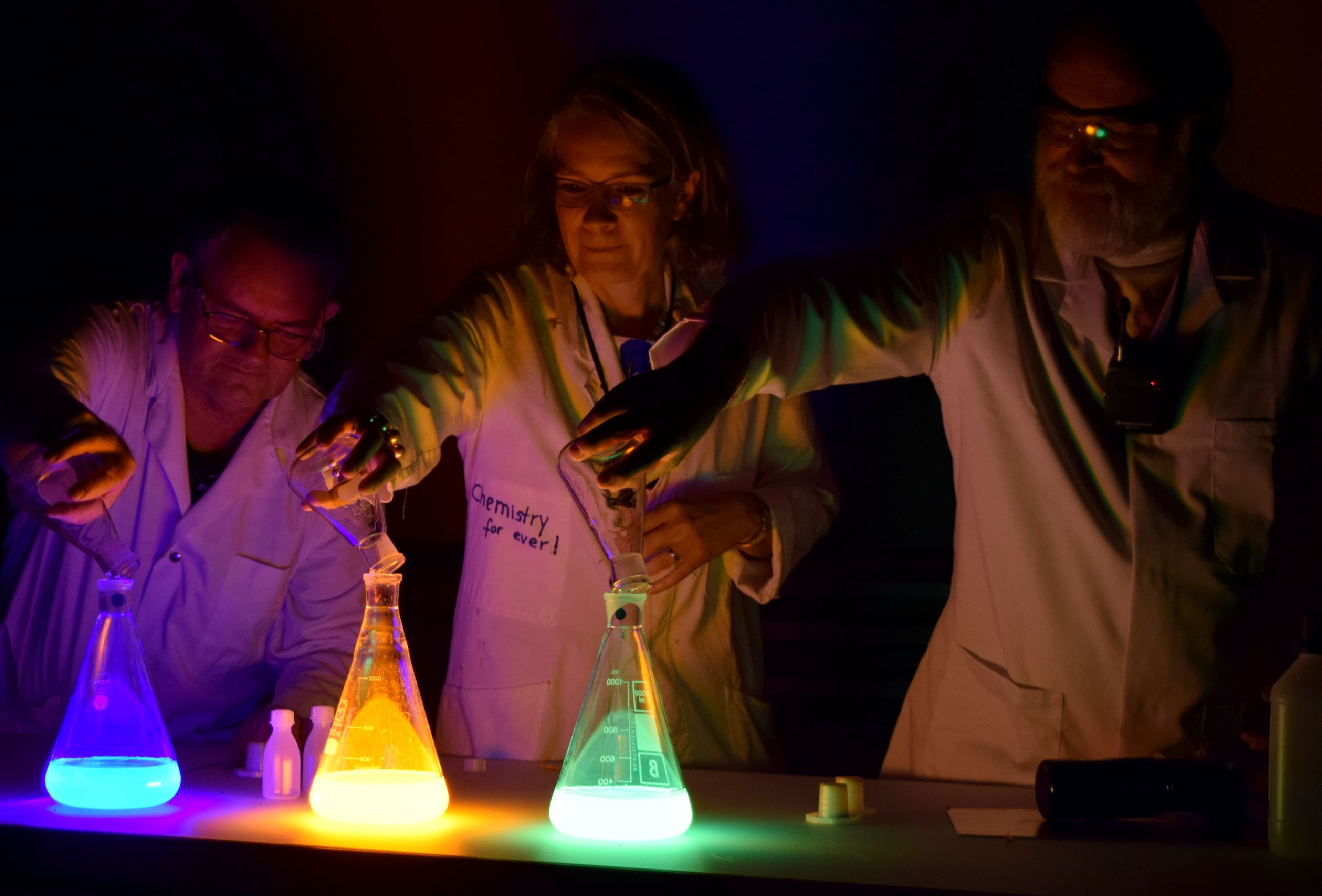 Three people working with fluorescent liquids