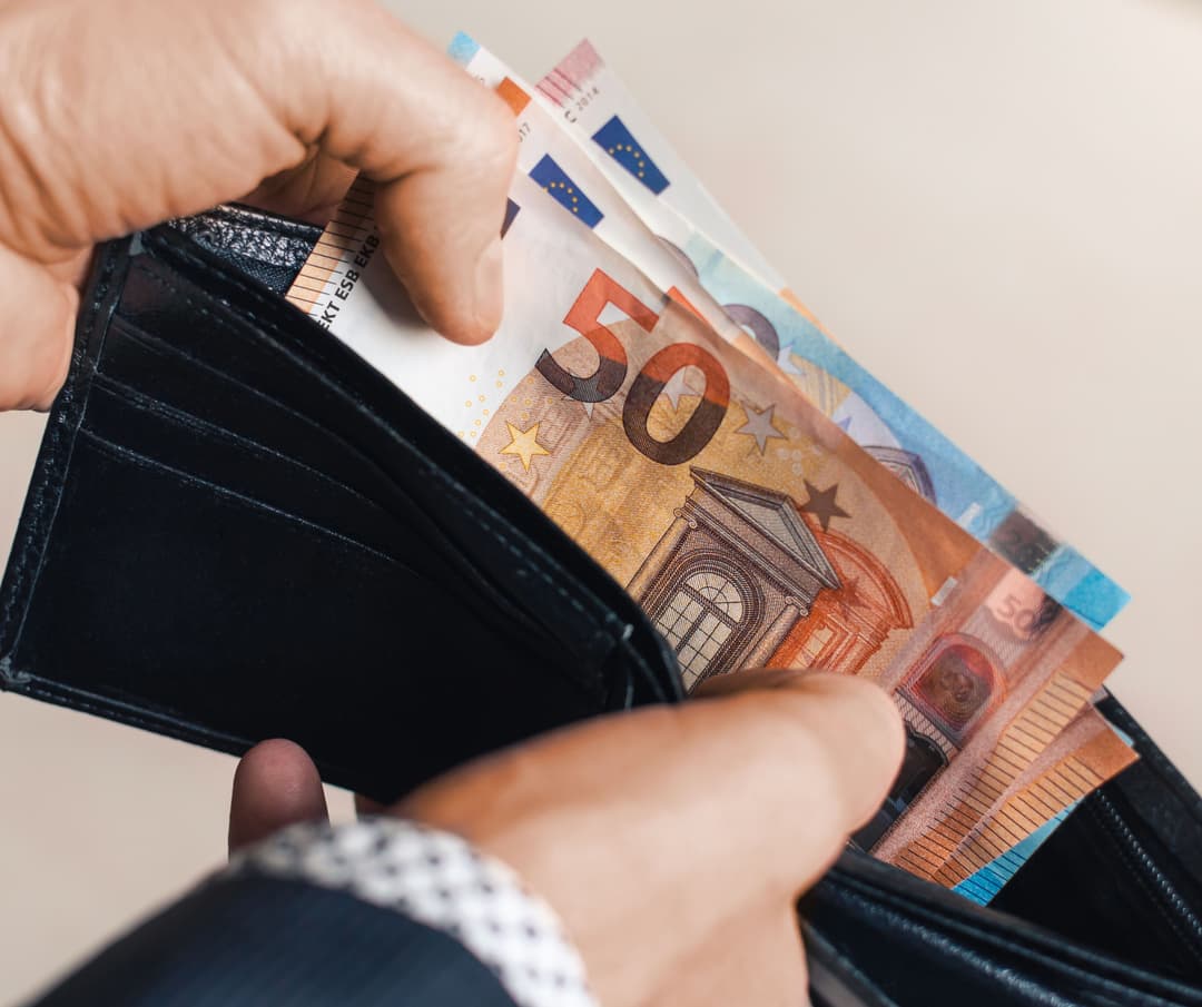 Hände ziehen mehrere Euro-Geldscheine aus einer schwarzen Lederbrieftasche