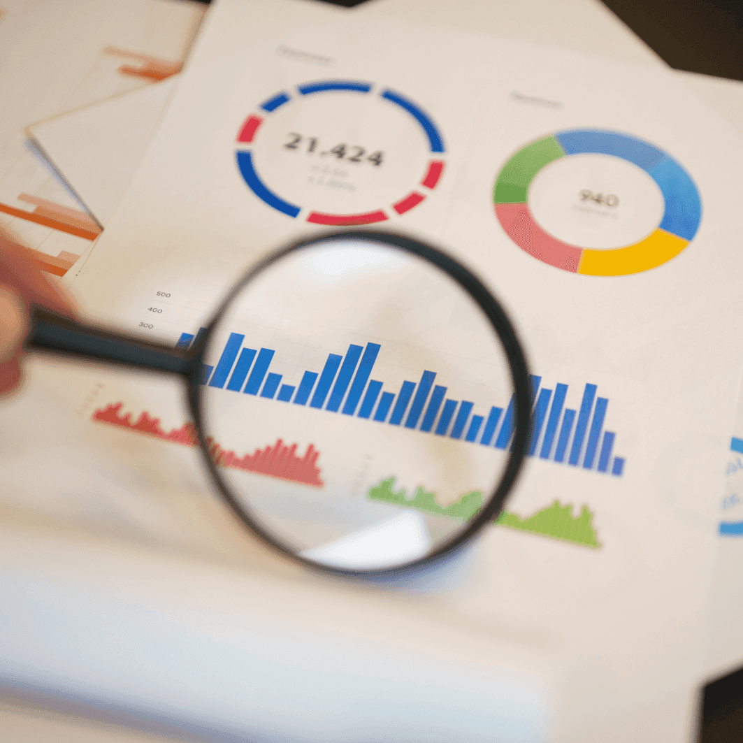 Hand hält Stift über ausgedruckte Diagramme und Tabellen mit Balken- und Liniendiagrammen auf Papier