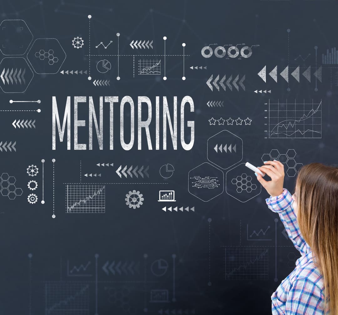 Frau mit langem Haar und kariertem Hemd steht vor einer Tafel mit dem Wort 'MENTORING' und verschiedenen grafischen Symbolen und Diagrammen