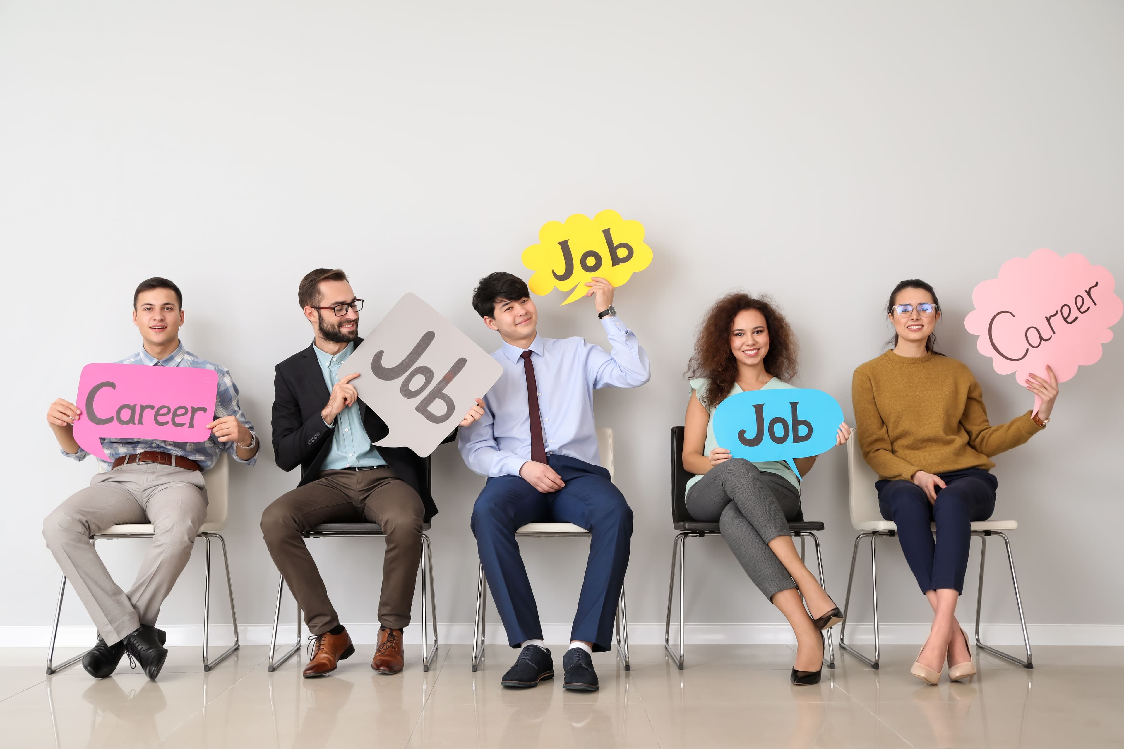 Fünf Personen in Businesskleidung sitzen auf Stühlen und halten bunte Schilder mit den Worten 'Job' und 'Career'